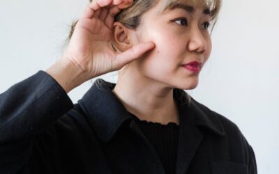 Portrait d'une femme asiatique avec la main sur l'oreille, symbolisant l'écoute ou l'attention, sur fond blanc.
