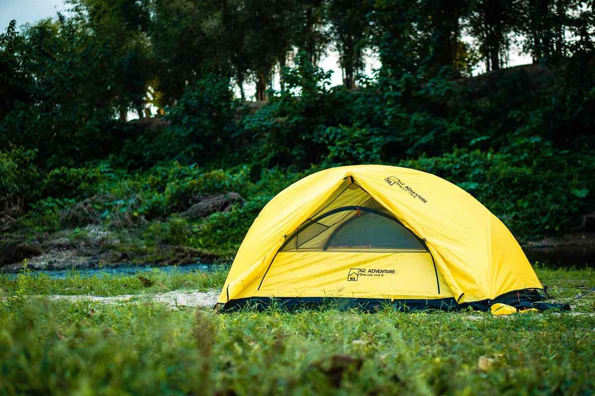 Tente jaune montée dans un terrain de camping entouré d'herbe et de forêt Tente jaune montée dans un terrain de camping entouré d'herbe et de forêt