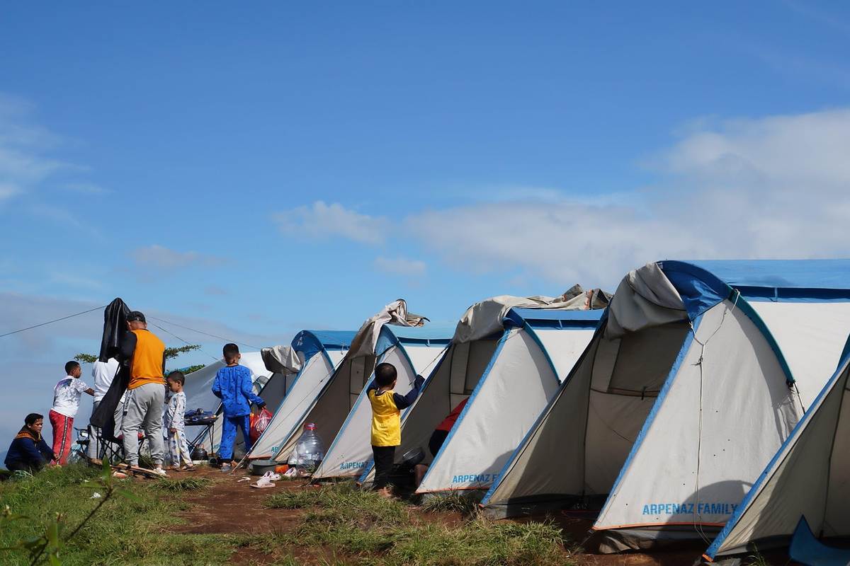 Plusieurs tentes de camping colorées installées dans un champ, des personnes autour Plusieurs tentes de camping colorées installées dans un champ, des personnes autour