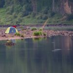 Une tente sur une plage, près d'un lac, avec un pêcheur