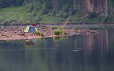 Une tente sur une plage, près d'un lac, avec un pêcheur