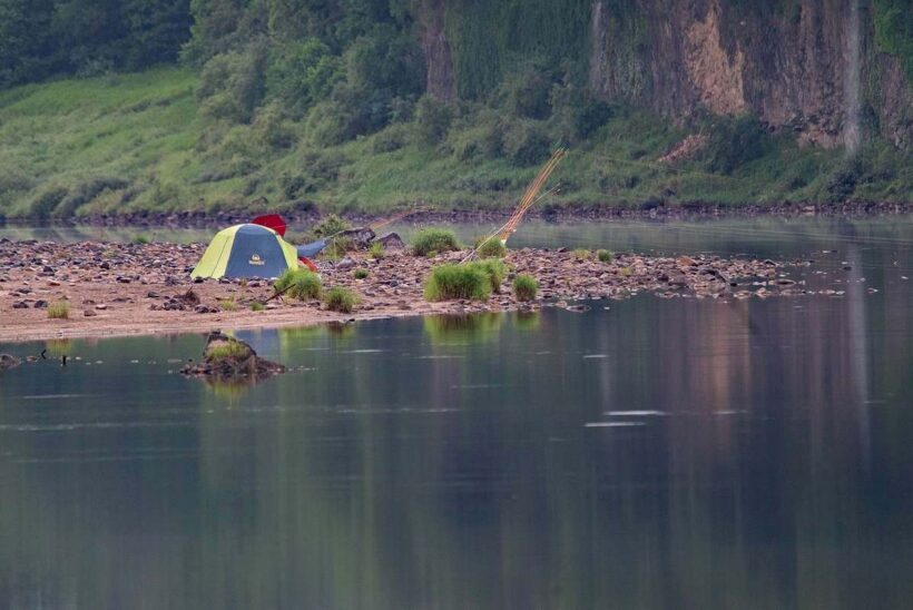 Une tente sur une plage, près d'un lac, avec un pêcheur