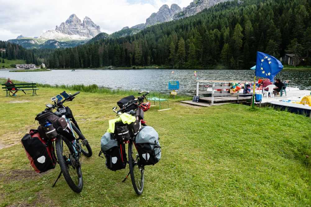 Deux vélos de voyage avec sacoches stationnés au bord d'un lac de montagne avec camping Deux vélos de voyage avec sacoches stationnés au bord d'un lac de montagne avec camping
